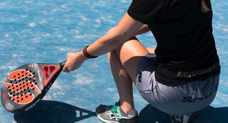 Padel player wearing athleisure sustainable sportswear on blue outdoor court